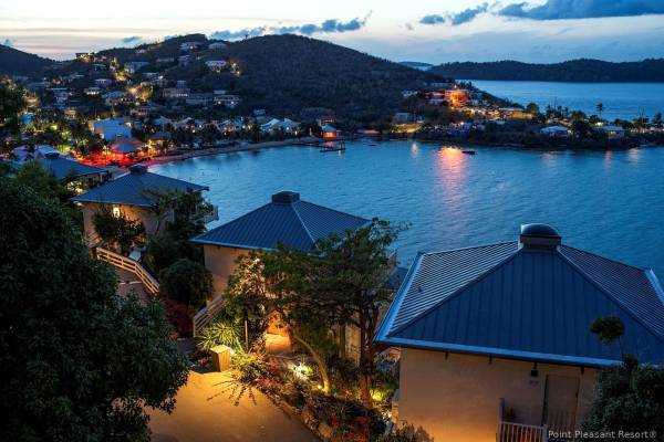 Evening view of Point Pleasant Resort in St. Thomas, U.S. Virgin Islands, featuring hillside villas illuminated with warm lights overlooking Water Bay, calm Caribbean waters reflecting shoreline lights, and surrounding hills beneath a twilight sky.