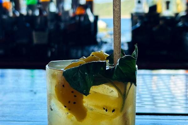 Tropical cocktail served at Lionfish Restaurant at Point Pleasant Resort in St. Thomas, U.S. Virgin Islands, featuring a chilled yellow drink garnished with fresh fruit and mint leaves on a bar overlooking Water Bay, with liquor bottles and Caribbean island views softly blurred in the background.