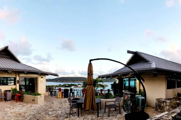 Exterior view of Point Pleasant Resort in St. Thomas, U.S. Virgin Islands, featuring the resort lobby and Lionfish Restaurant buildings, outdoor patio seating, Caribbean views of Water Bay, tropical landscaping, and U.S. Virgin Islands and American flags flying above the property at sunset.