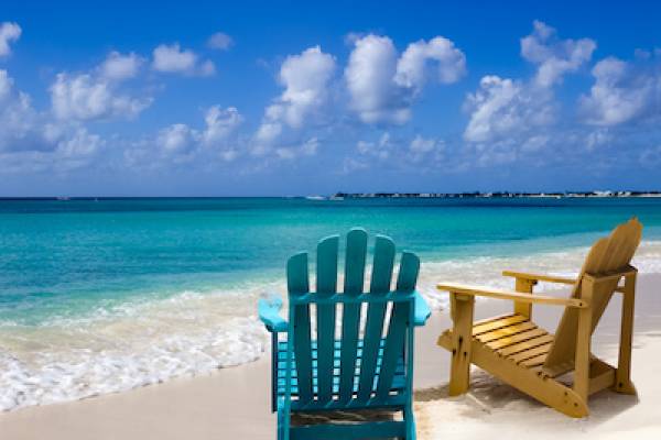 two beach chairs in the sand with blue waves rolling in on a sunny day