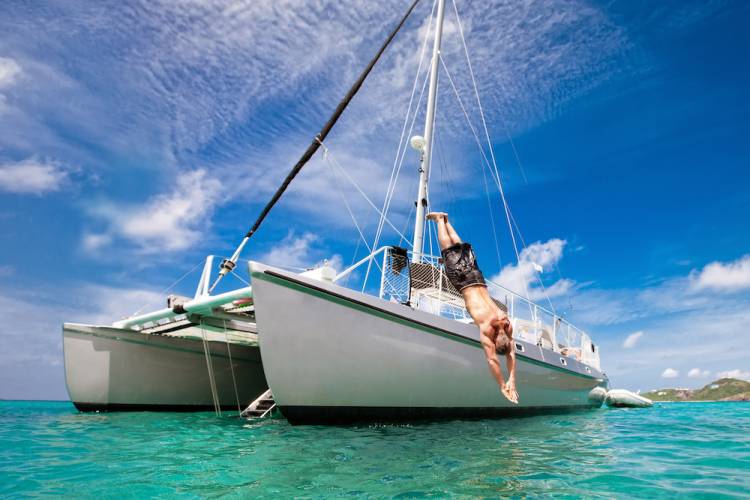 a man diving off of the deck of a catamaran into the turquoise waters of the Caribbean