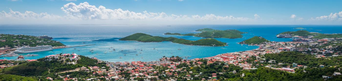 Beautiful colorful and panoramic image of St Thomas. Blue sky, White clouds, sea, mountains, houses and cruise ports with ships in the background.